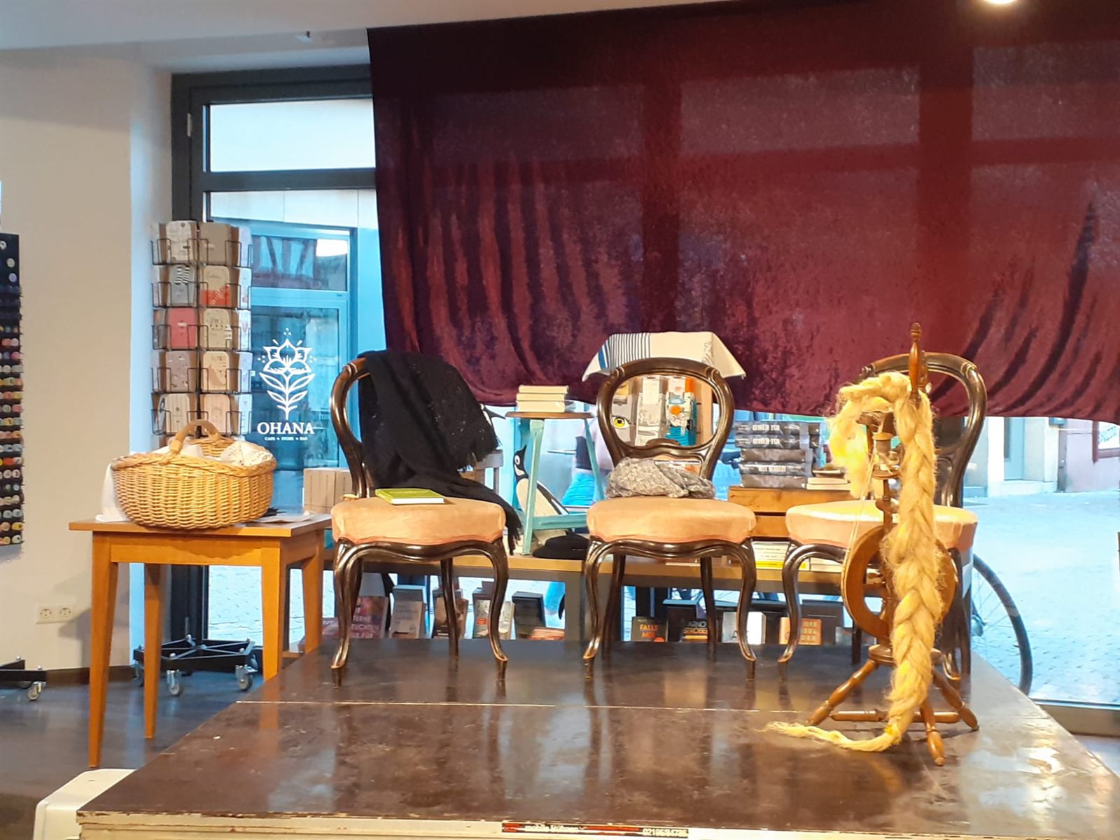 Drei Polsterstühle auf einem niedrigen Holzpodest, rechts ein Spinnrad mit heller Wolle, links ein Tisch mit Weidenkorb