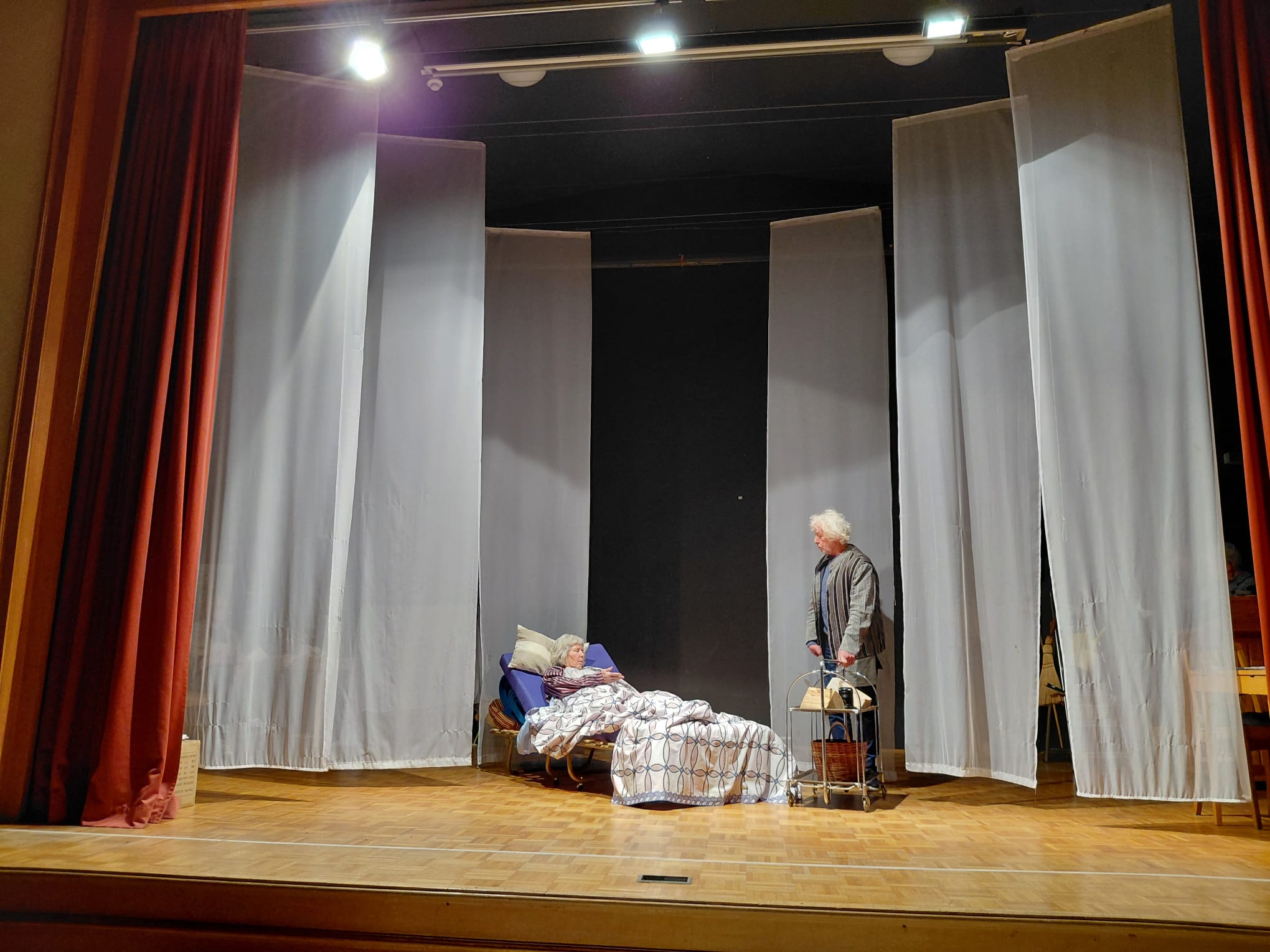 Bühne mit rotem Vorhang, zwei Spielende der Theatergruppe in einer Szene