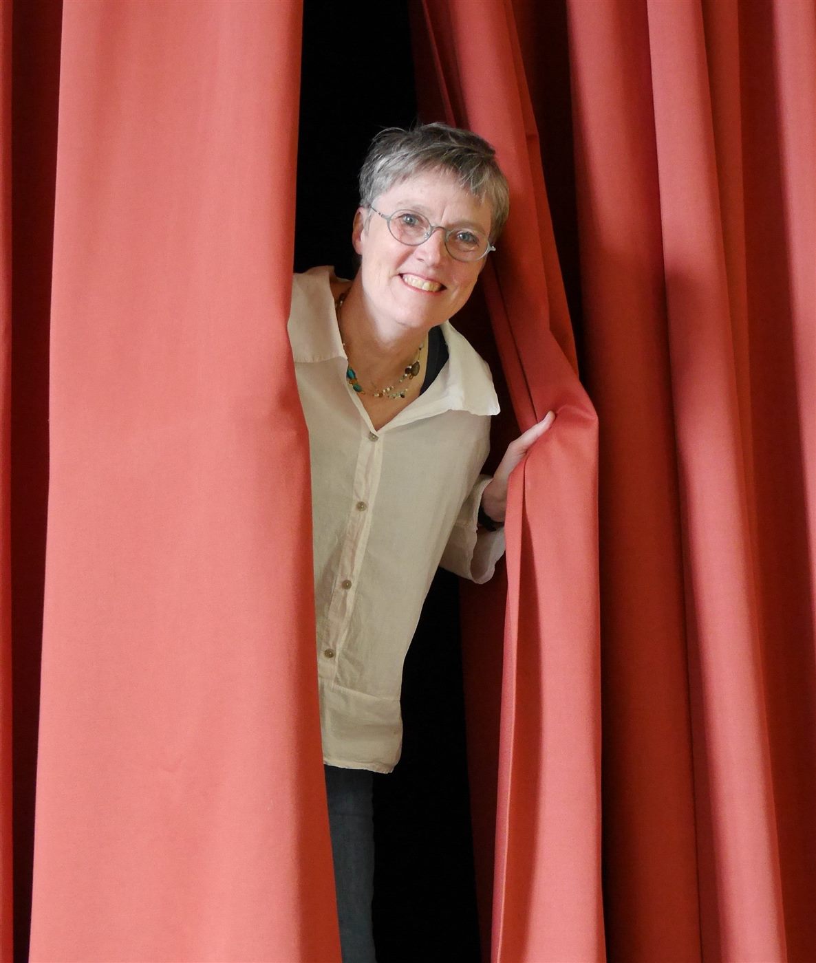 Wiebke Stölting schaut zwischen roten Theatervorhängen hervor